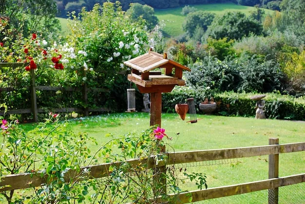 Garden with a wooden fence, a bird table on a post and flowering shrubs around a lawn